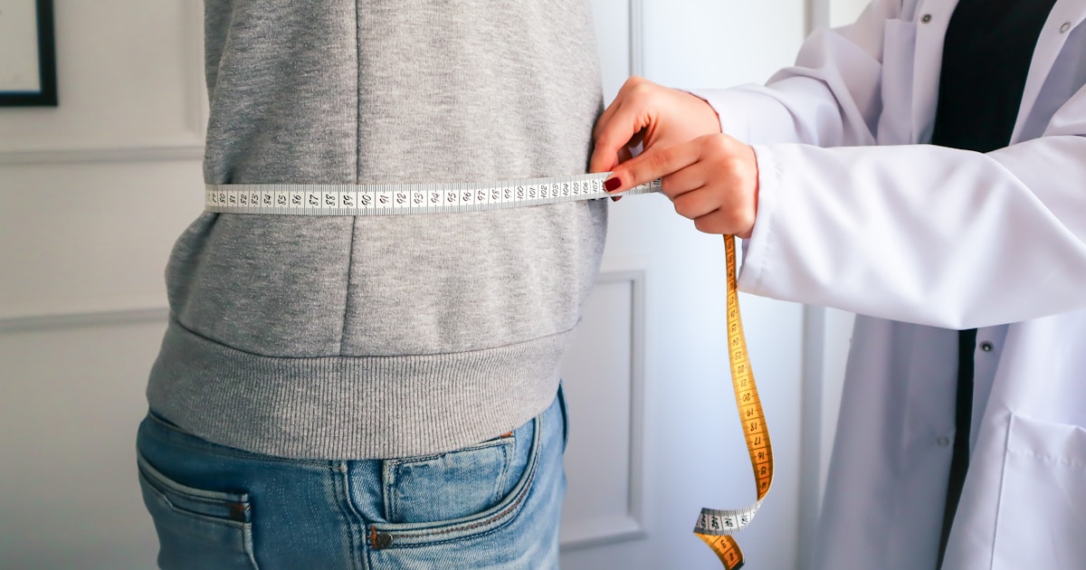 Clinician measuring a patient's waist circumference with a tape measure during a weight management review