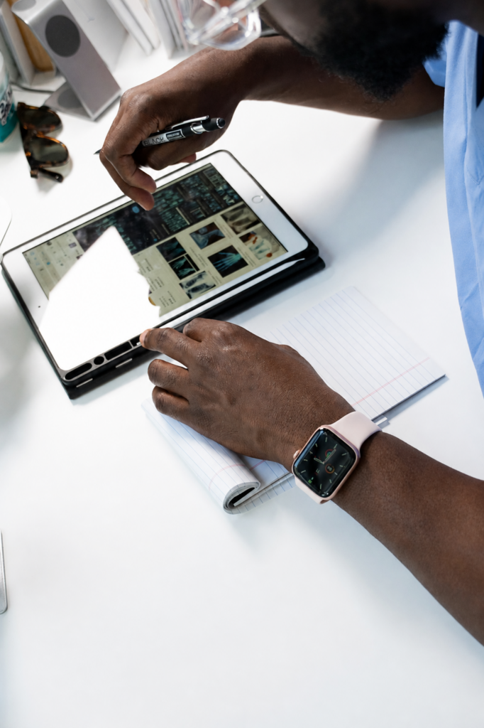 Healthcare worker in blue scrubs reviewing images on a tablet at a white desk, notepad and pen nearby.