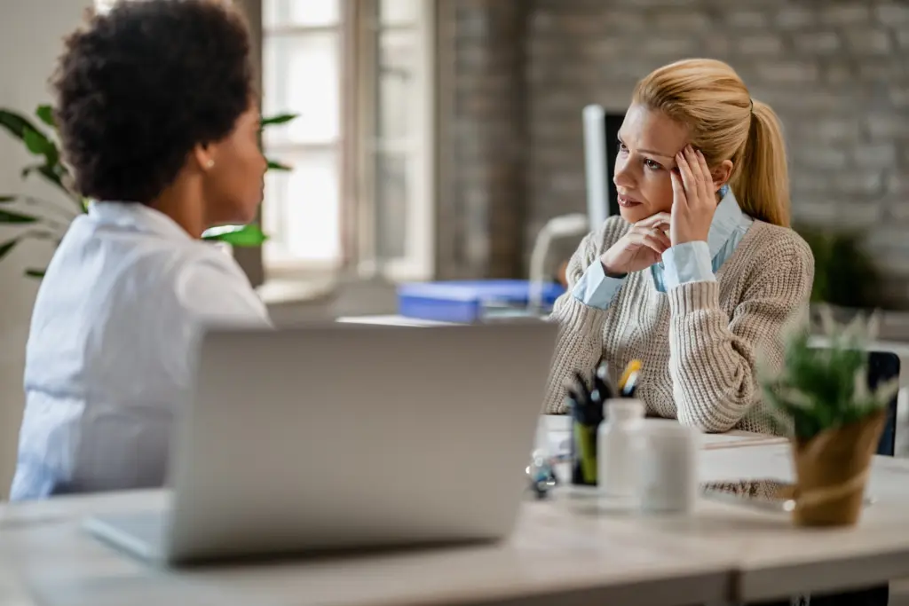Mid adult woman feeling worried while talking to african american doctor during medical appointment.