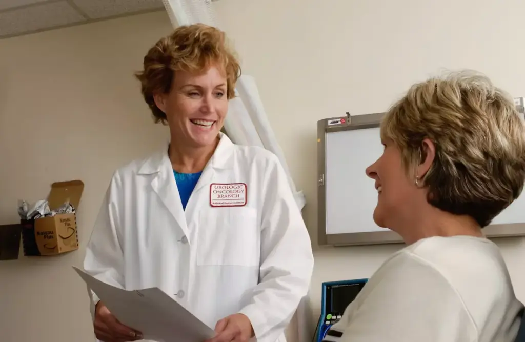 Nurse wearing a white uniform speaking with a patient.
