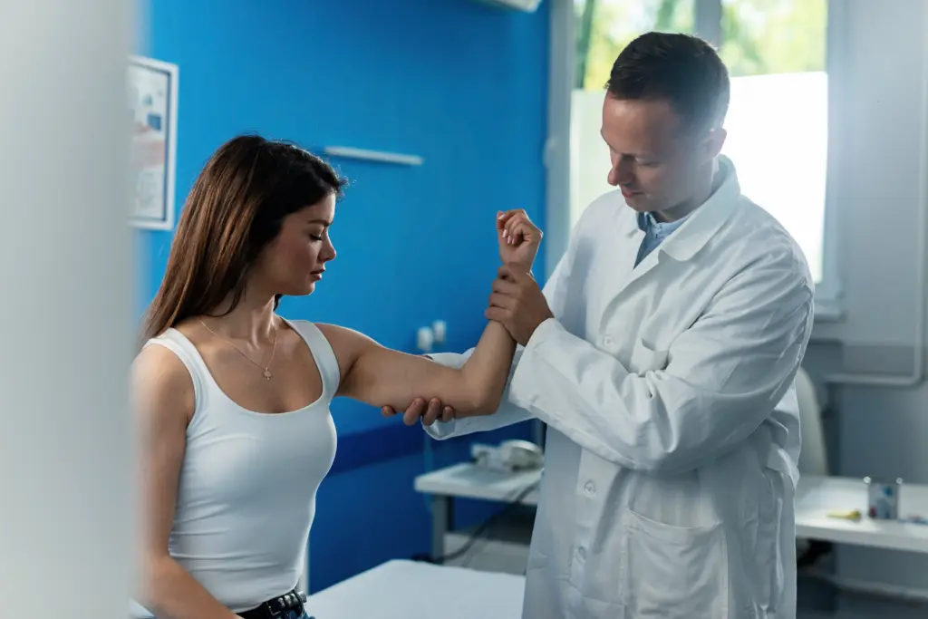 Young woman getting her arm examined by male orthopedist medical appointment at clinic